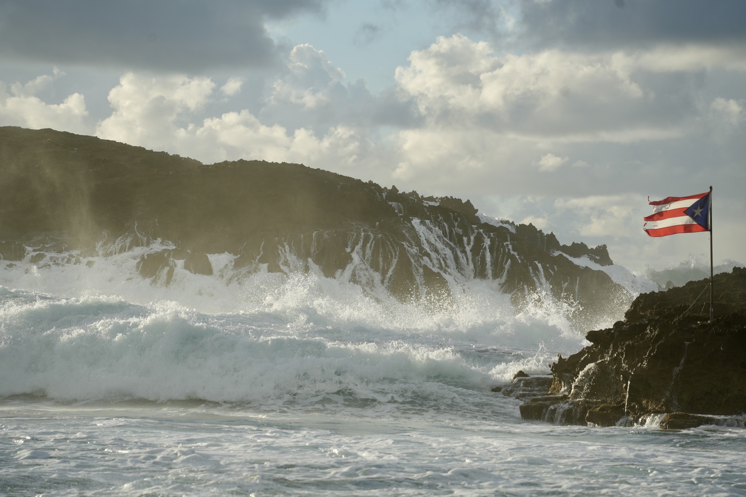 Waves breaking along the rocky Caribbean coastline near a Puerto Rican flag