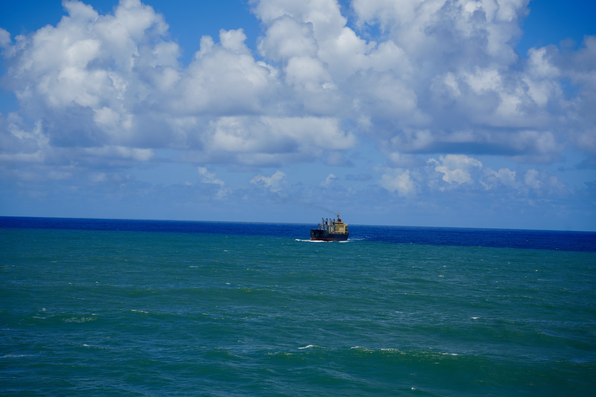 A distant cargo vessel crossing a wide blue horizon